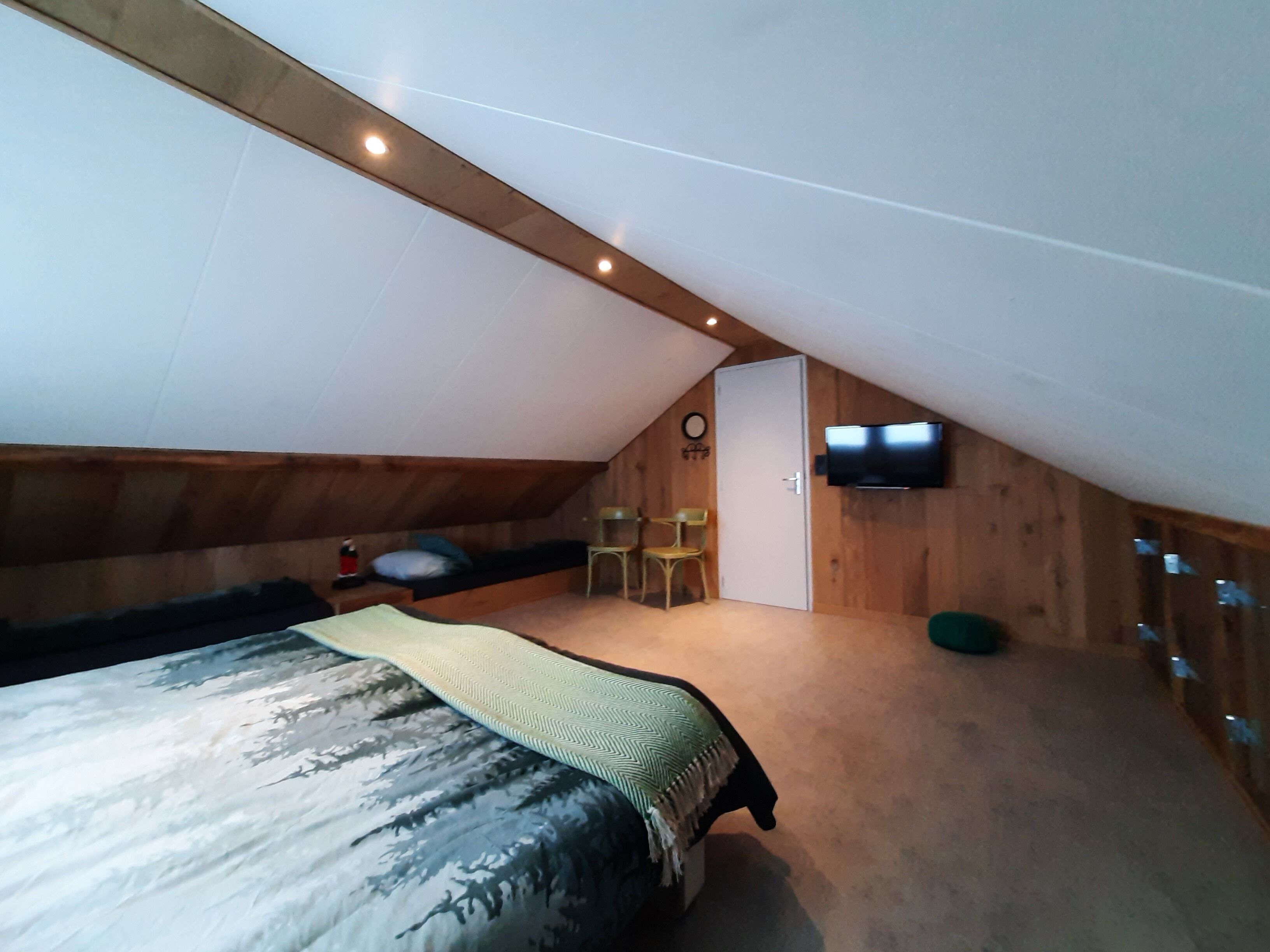 A cozy attic bedroom with a bed, a TV, and a small seating area.