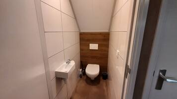 Une petite salle de bain aux murs recouverts de carreaux blancs, avec un mur d’accent en bois, un lavabo blanc et des toilettes.