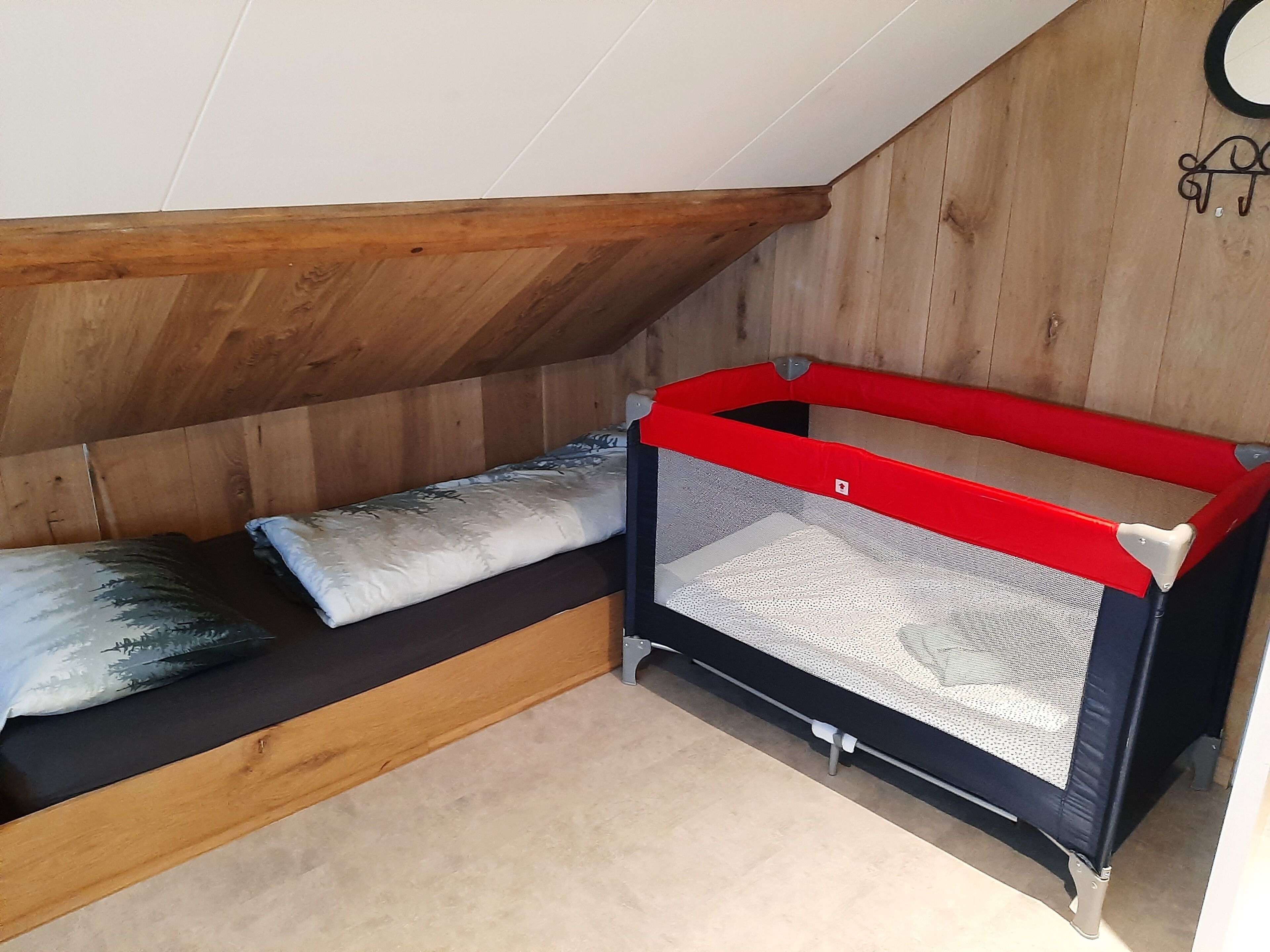 A small, enclosed sleeping area with a wooden ceiling and sloped walls, featuring a red and black baby crib and a cushioned bench.