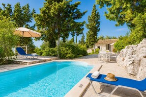 A swimming pool with lounge chairs and a table, surrounded by trees and a stone wall. - Millers Cottage Large Private Pool, A/C, WiFi (Paxi)