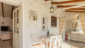 Una habitación rústica con pared de piedra, techo de madera, una mesa de comedor con sillas, un televisor y un baño con lavabo y espejo.