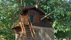 Ein rustikales Holzbaumhaus mit einer Holztreppe, die zu einer Plattform führt.