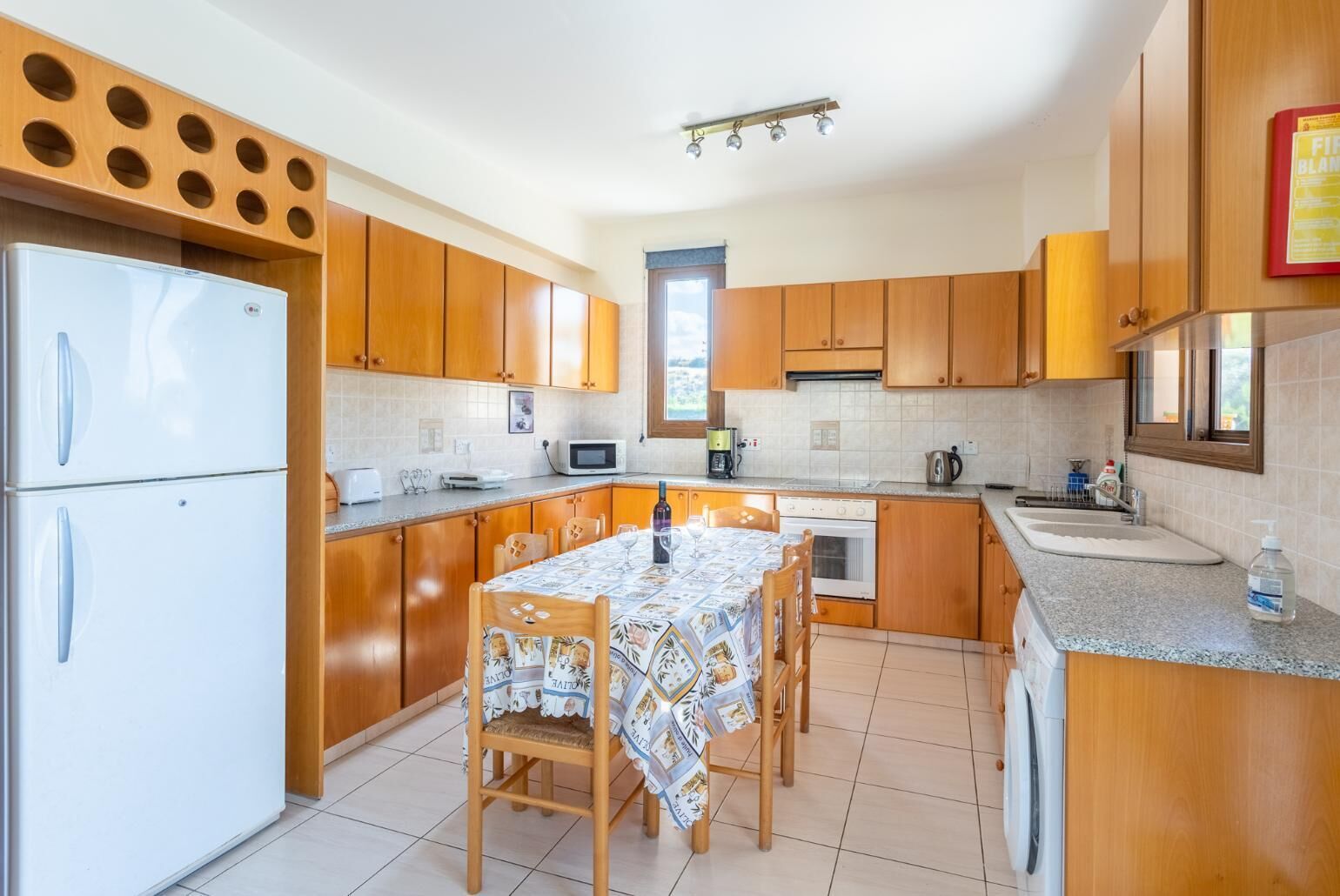 Una cocina con armarios de madera, un refrigerador blanco, una mesa de comedor con sillas, un microondas y un lavamanos.