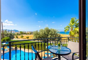 A balcony with a pool, a table with wine glasses, and a view of the beach and mountains. - Villa Halima Georgios (Latchi)