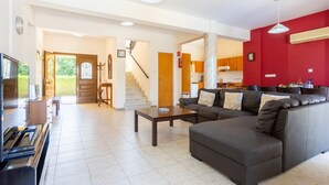 Ein geräumiger Wohnbereich mit einer Couch, einem Couchtisch und einem Fernseher. Eine Treppe führt zu einer Küche mit roten Wänden und einem Esstisch.
