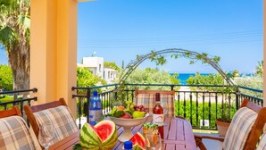 Ein Holztisch mit Obstschale, einer Wasserflasche und einer Weinflasche auf einem Balkon mit Blick aufs Meer.