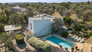 Una villa con piscina, muros de piedra y jardín con diversas plantas y flores.