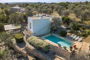 A villa with a swimming pool, stone walls, and a garden with various plants and flowers.