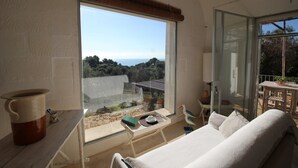Un balcón con un sofá blanco, una mesita y vistas al mar y a los árboles.