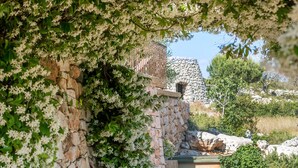 Un sendero de piedra conduce a un edificio de piedra de aspecto rústico, rodeado de exuberante follaje y plantas florecientes.