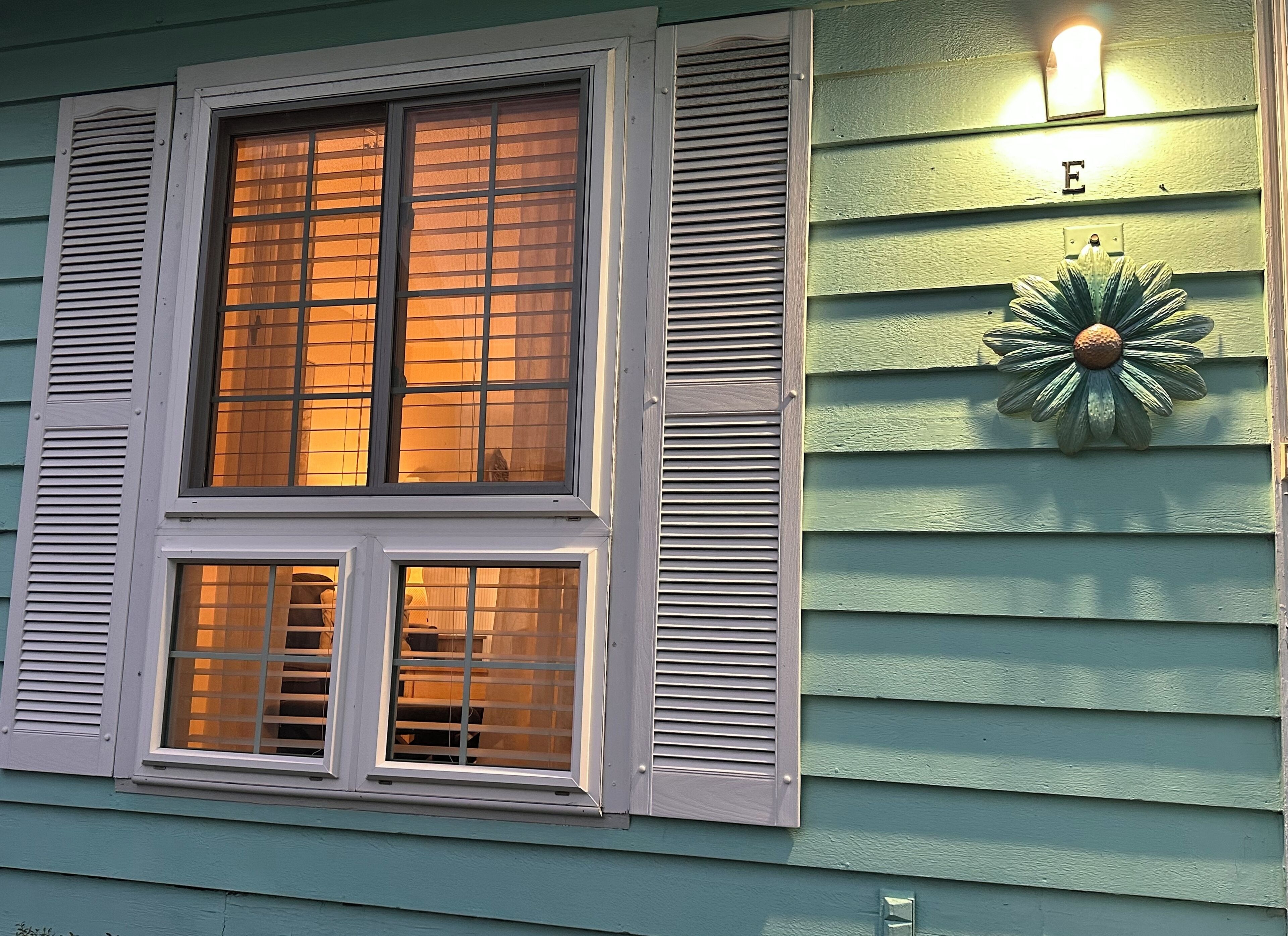 Une maison avec deux fenêtres, chacune dotée de volets, et un luminaire décoratif fixé au mur.