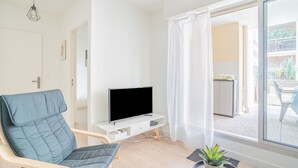 A modern living room with a flat-screen TV on a white stand, a blue cushioned chair, a small potted plant, and a sliding glass door leading to an outdoor area.