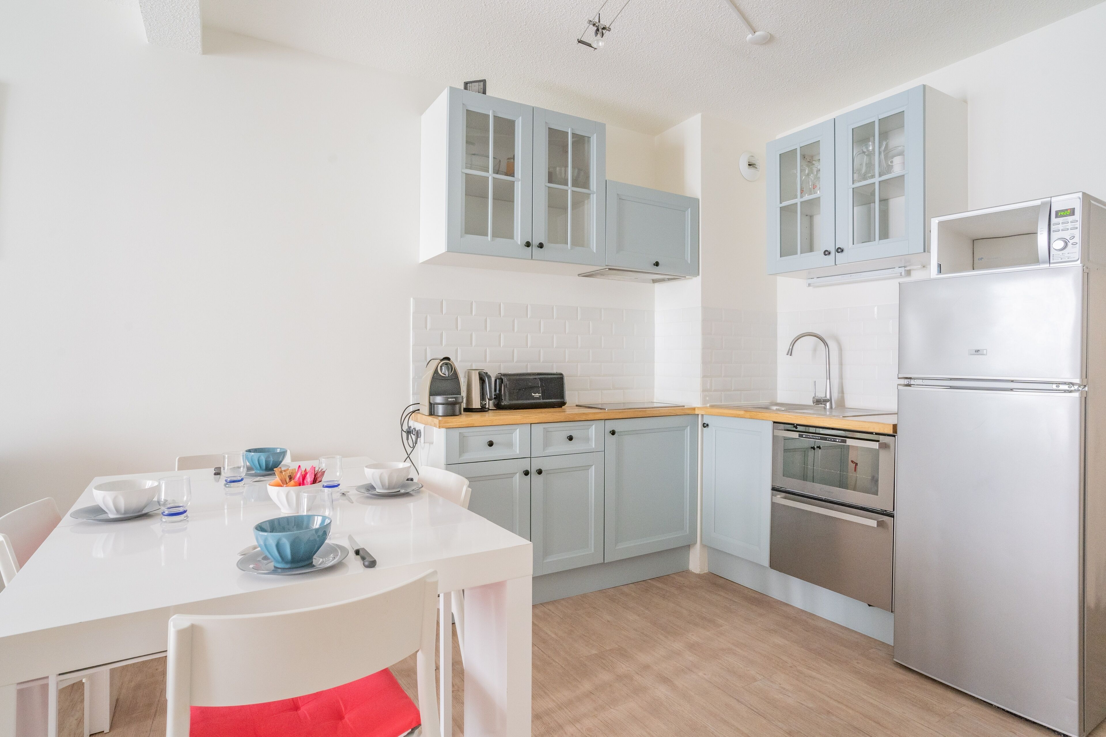 A modern kitchen with light blue cabinets, a white countertop, and stainless steel appliances including a microwave and oven.