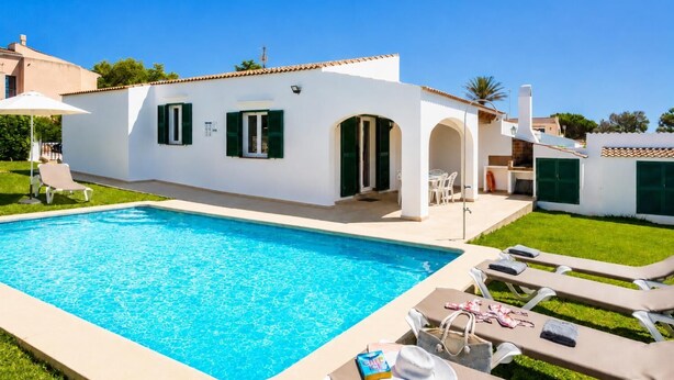 Un área junto a la piscina con piscina, sillas de descanso y un edificio blanco con contraventanas verdes.