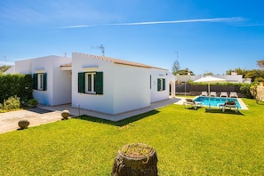 A white villa with a swimming pool, green shutters, and a clear blue sky.
