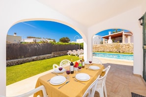 A dining area with a table set for four, outdoor pool, and a view of the surrounding landscape.