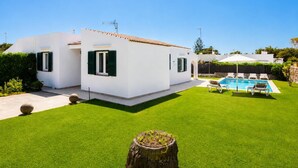 Una casa moderna blanca con piscina y césped bien cuidado.