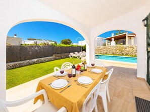 Un espace repas avec une table dressée pour quatre personnes, une piscine extérieure et une vue sur l’espace piscine.