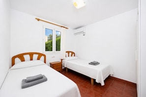 Una habitación con dos camas, una ventana con cortinas, un equipo de aire acondicionado y una mesita de noche.