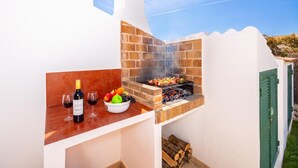 Un patio con una parrilla de ladrillo, una botella de vino, copas y un cuenco con fruta.