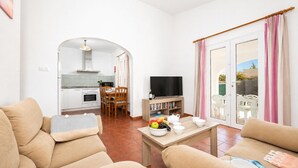 Una sala de estar con un sofá, un televisor, una mesa de comedor con sillas y una cocina al fondo.