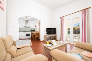 Una sala de estar con un sofá, un televisor, una mesa de comedor con sillas y una cocina al fondo.