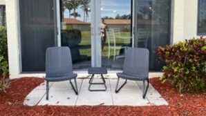 Un espace patio avec deux chaises et une petite table, une porte-fenêtre coulissante et un paillis rouge recouvrant le sol.