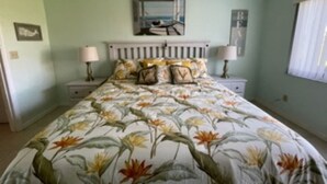 Une chambre à coucher avec une couvre-lit à motifs floraux, une tête de lit blanche, deux lampes de chevet et un tableau encadré au mur.