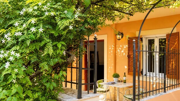 A patio with a table and chairs, a potted plant, and a door leading to the interior. - Foteini Apartment - Two Bedroom Apartment, Sleeps 2 (Corfu)