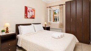 A bedroom with a bed, nightstands, a window with curtains, a wardrobe, and a painting on the wall. - Foteini Apartment - Two Bedroom Apartment, Sleeps 2 (Corfu)