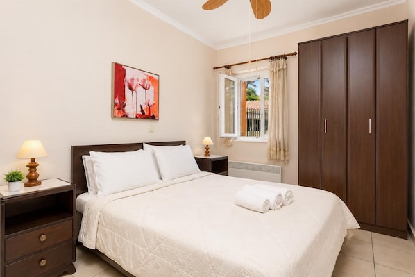 Quarto com cama, mesas de cabeceira, janela com cortinas, guarda-roupa e um quadro na parede.