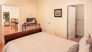 A bedroom with a large bed, a TV on a desk, and a door leading to another room.