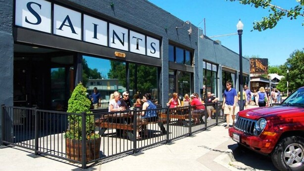 A restaurant named 'SAINTS' with outdoor seating and a red vehicle parked outside.