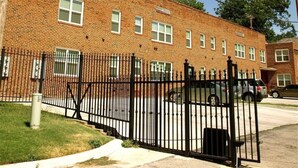 A brick building with multiple windows and a black metal fence.