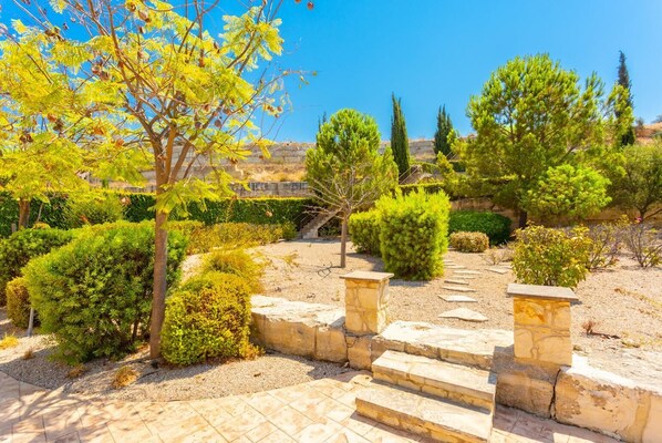 Um jardim com degraus de pedra que levam a uma área de observação, rodeado por arbustos e árvores.
