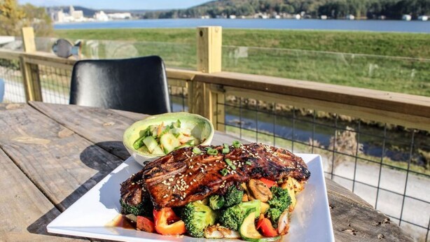 Comida sobre una mesa de madera con vistas a un lago y vegetación.