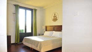Ein Schlafzimmer mit Bett, Nachttisch, einem Fenster mit Vorhängen, einer Wanddekoration und einer Tür.