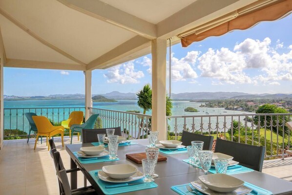 A dining area with a table set for four, overlooking a scenic view of a body of water and distant land.