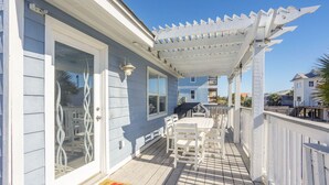 A covered porch with a white pergola, a dining table and chairs, and a barbecue grill.