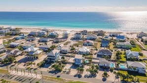 An aerial view of a coastal residential area with houses, a beach, and a clear sky.