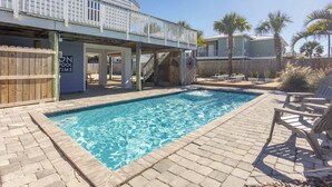 A swimming pool with a wooden deck, lounge chairs, and a covered area with a sign reading "ON POOL TIME".