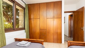 Un dormitorio con dos camas, armarios de madera, una ventana con cortinas y un radiador.