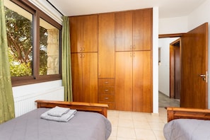 A bedroom with two beds, wooden wardrobes, a window with curtains, and a radiator. - Villa Heaven - Three Bedroom Villa, Sleeps 6 (Peristerona)