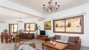 Amplia sala de estar con mesa de comedor, sofás, televisor y ventanas grandes con vista a un paisaje rocoso.