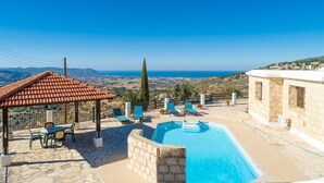 Un área de piscina en la azotea con vistas despejadas del paisaje, muros de piedra y un pérgola con sillas.