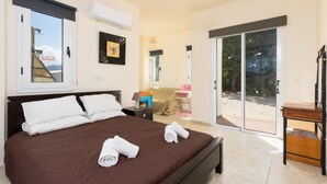 Une chambre à coucher avec un grand lit, une table de chevet, une lampe, une chaise et une porte-fenêtre coulissante donnant sur un balcon.