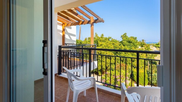 Un balcon agrémenté d’une pergola, de chaises en plastique blanc et offrant une vue sur la verdure et une route.