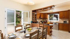 Une cuisine moderne avec des meubles en bois, un coin repas avec une table dressée pour quatre personnes et une grande fenêtre donnant sur un jardin.