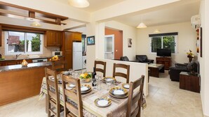 Une cuisine moderne avec des meubles en bois, un coin repas avec une table dressée pour quatre personnes, et un salon avec un canapé et un téléviseur.