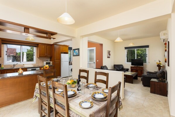 A modern kitchen with wooden cabinets, a dining area with a table set for four, and a living room with a sofa and TV. - Villa Kleopatra - Four Bedroom Villa, Sleeps 8 (Polis)